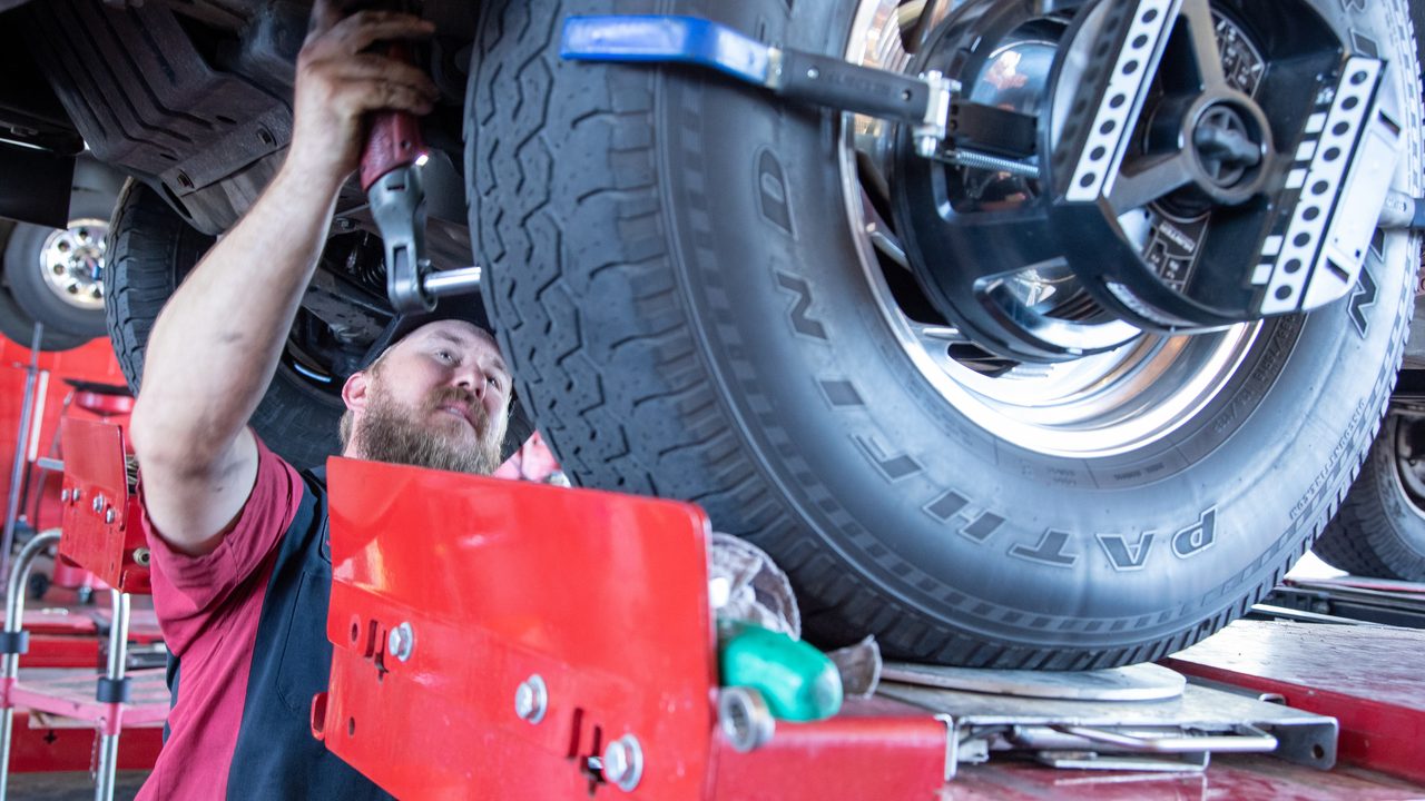 A technician uses a ratchet tool to adjust the suspension during a wheel alignment on a vehicle