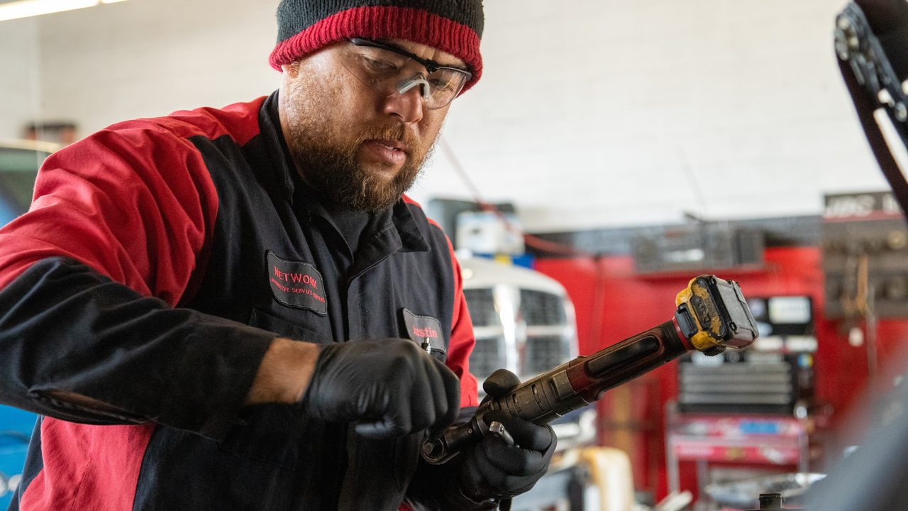 A technician adjusts a cordless ratchet while working under the hood in a service bay