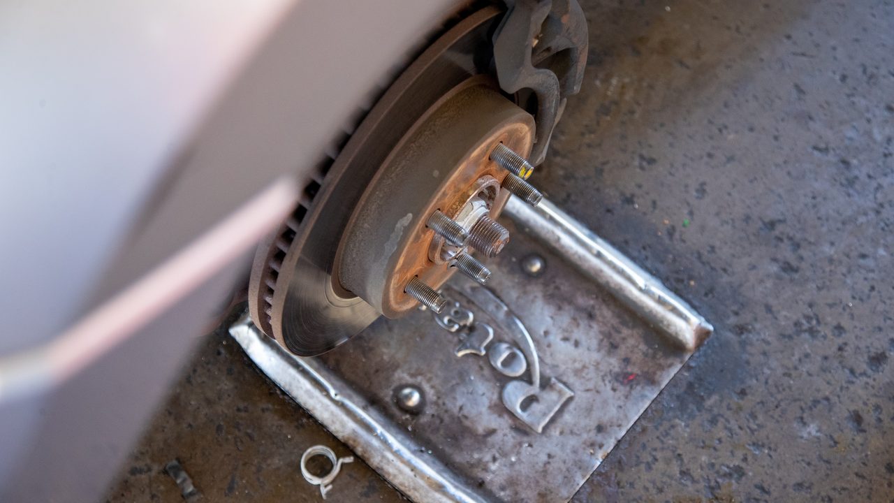 A vehicle sits with its wheel removed, exposing the brake rotor and caliper above a shop lift