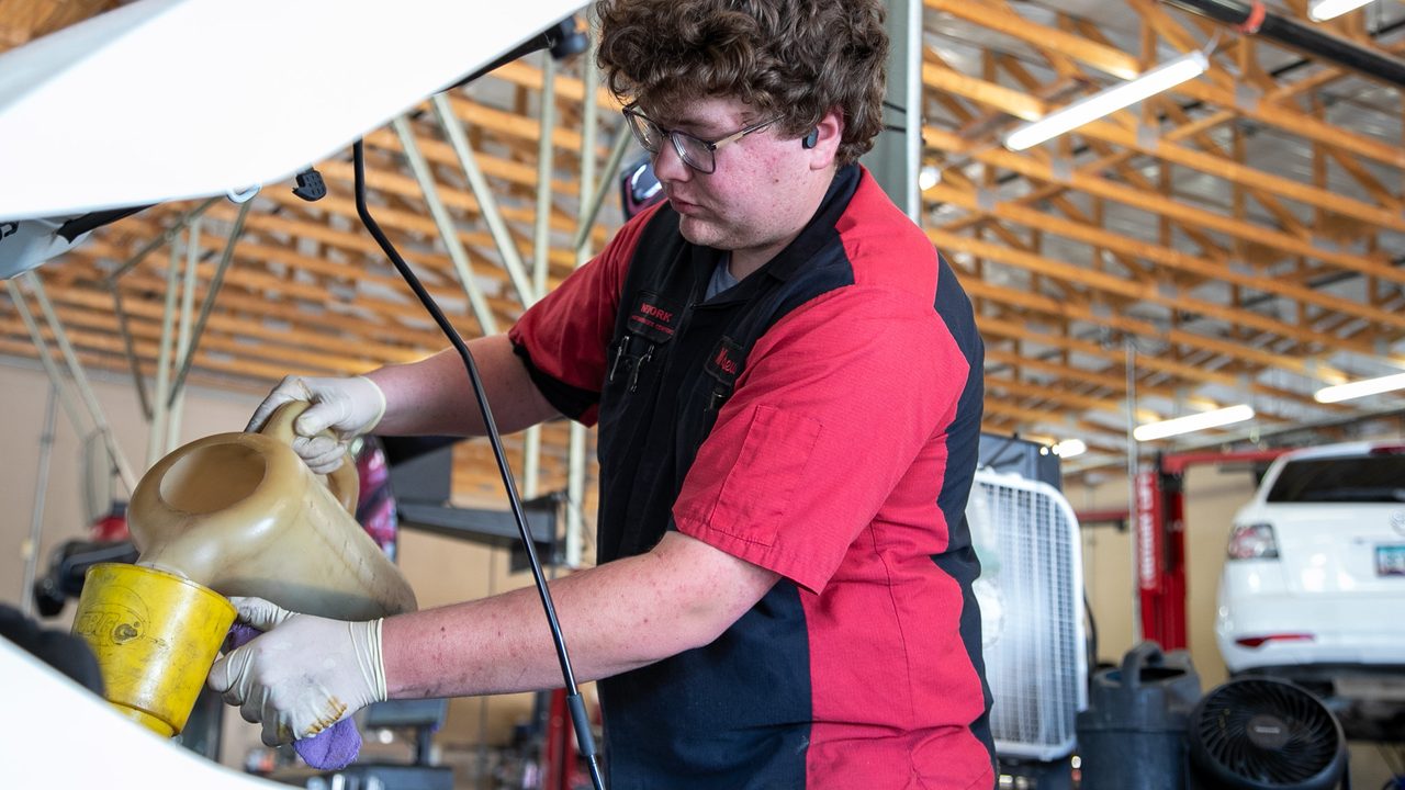 A technician pours fresh motor oil into an engine bay using a funnel during an oil change service