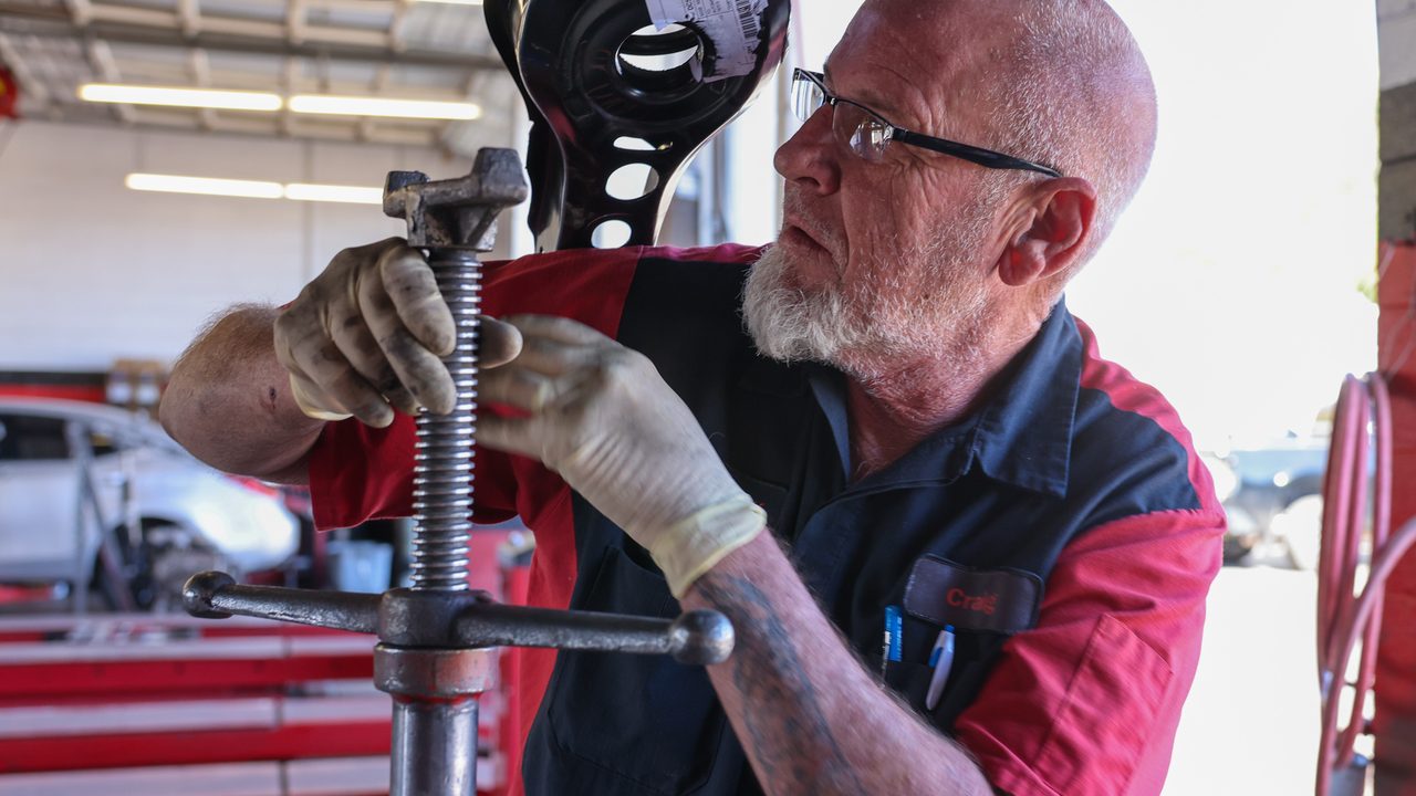 A technician adjusts an underhoist support stand while working on a vehicle's suspension in a service bay