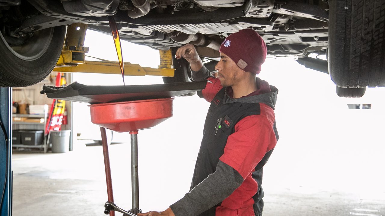 A technician performs an oil change, catching draining engine oil beneath a vehicle raised on a lift