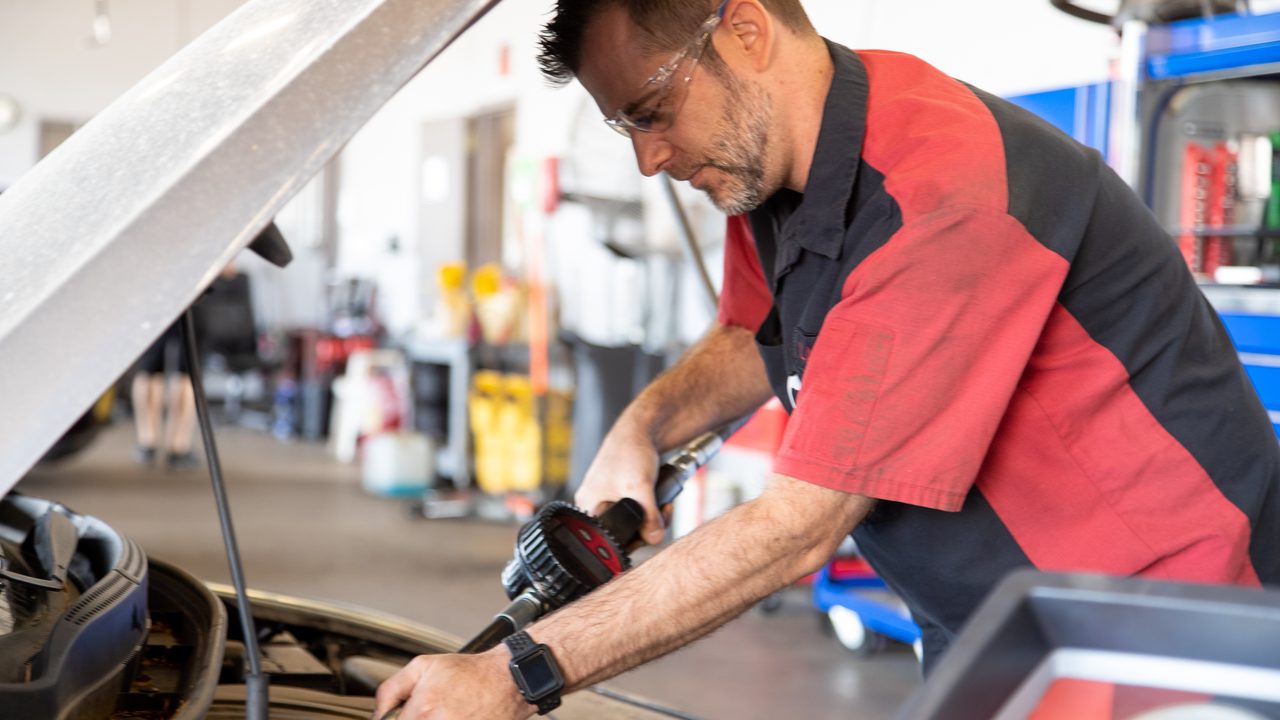 A technician fills an engine with motor oil using a fluid dispensing nozzle in a service bay