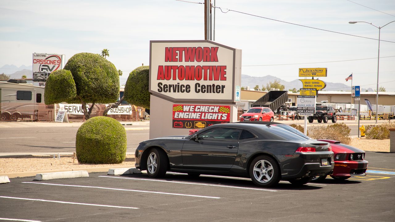 A gray sports car is parked in front of an automotive service center sign