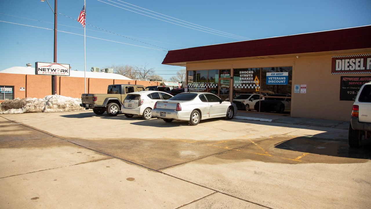 Several vehicles are parked outside an auto repair shop storefront on a clear, sunny day