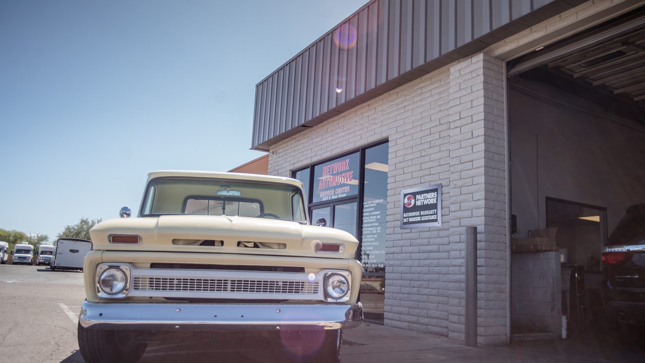 A vintage pickup truck is parked outside the storefront and service bay of an automotive repair shop
