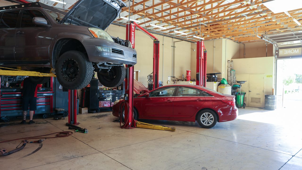 A technician works near a large toolbox beneath an SUV raised on a lift in a service bay