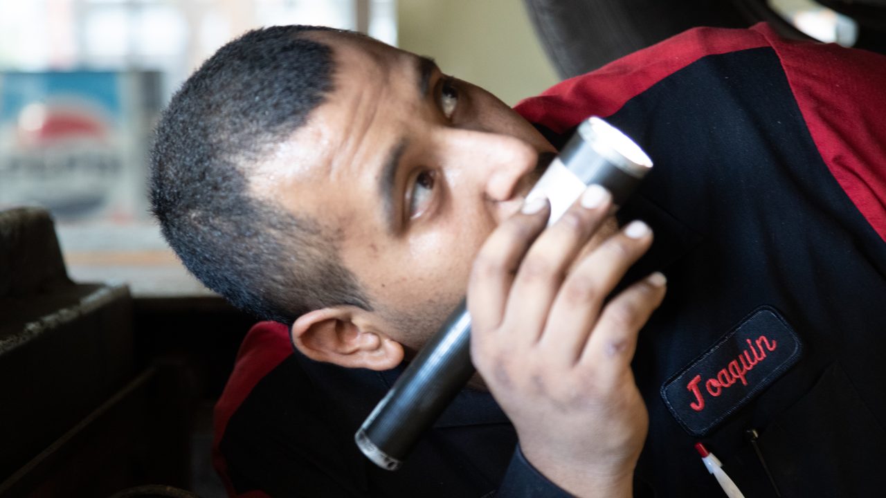 A technician uses a flashlight to inspect the undercarriage of a vehicle on a lift