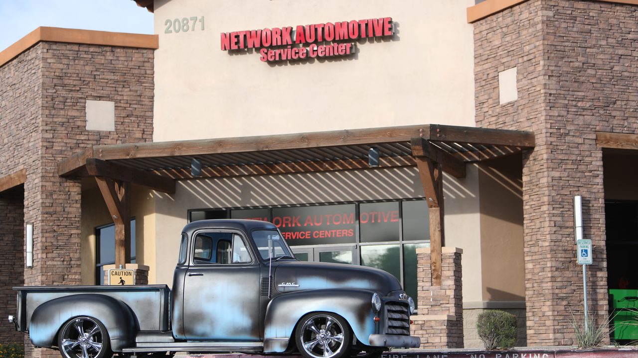 A customized vintage pickup truck parked in front of an automotive repair shop storefront