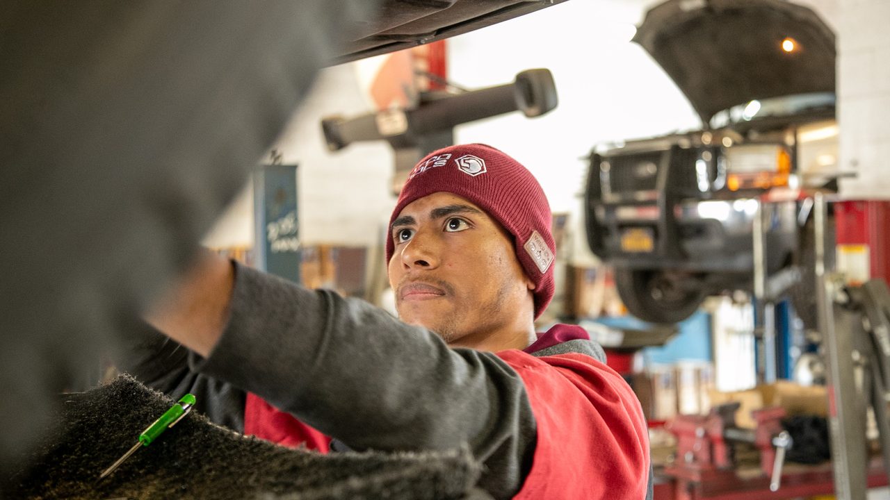 A technician works underneath a raised vehicle in an auto repair service bay