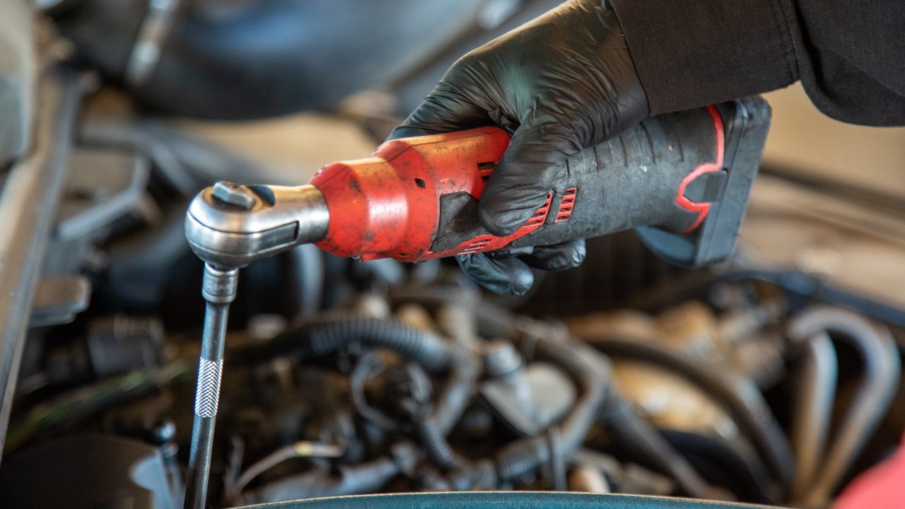A technician uses a cordless electric ratchet to work inside a vehicle's engine bay