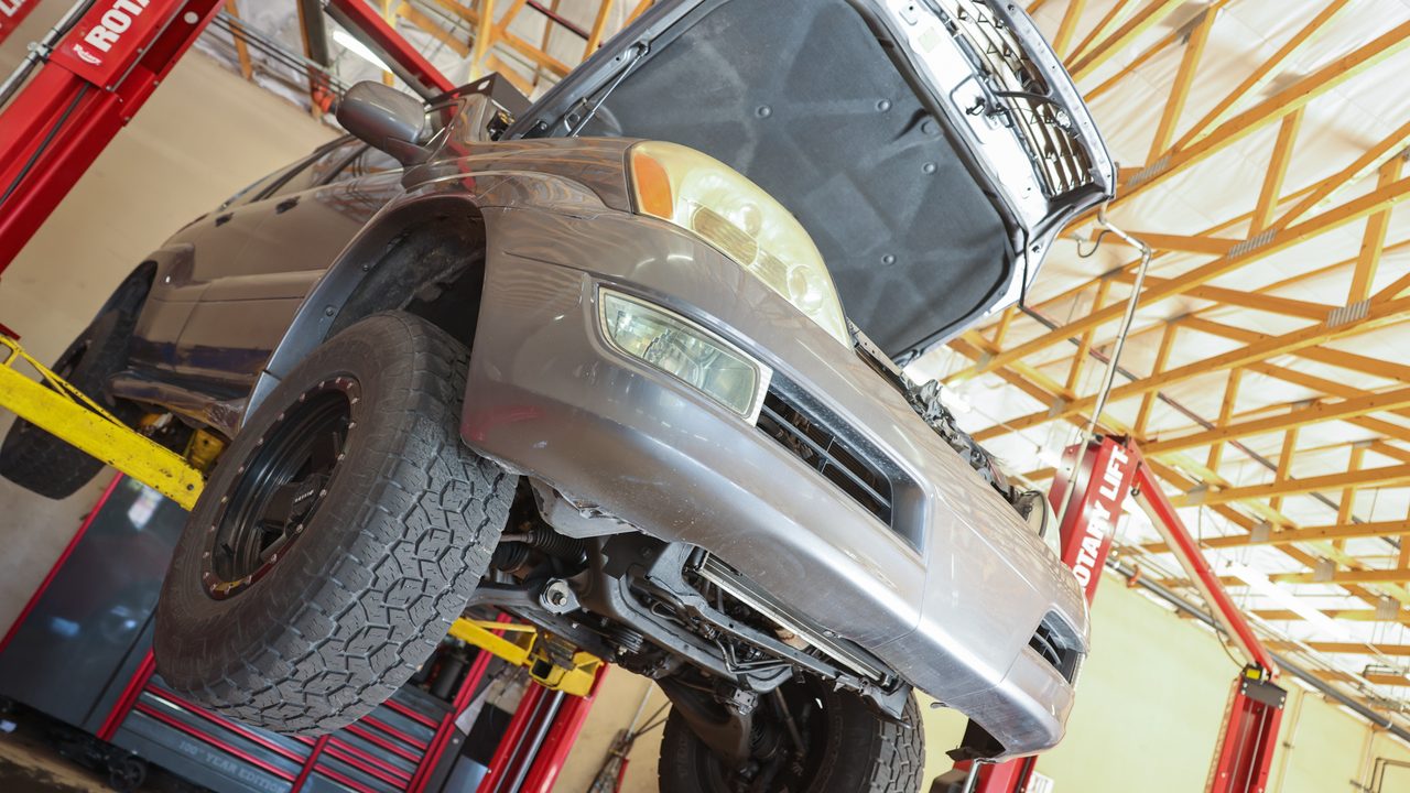 An SUV with an open hood is raised on a hydraulic lift inside an auto repair service bay