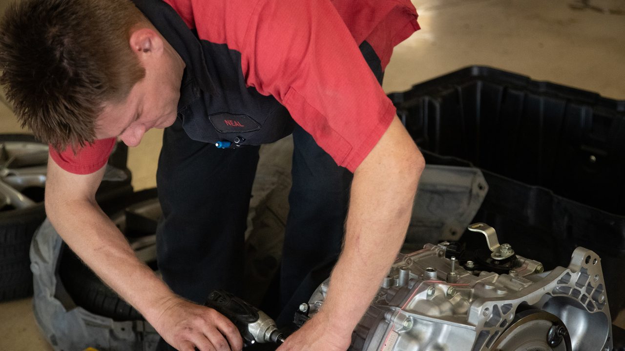 A technician uses a power tool to assemble or service a vehicle transmission in a shop