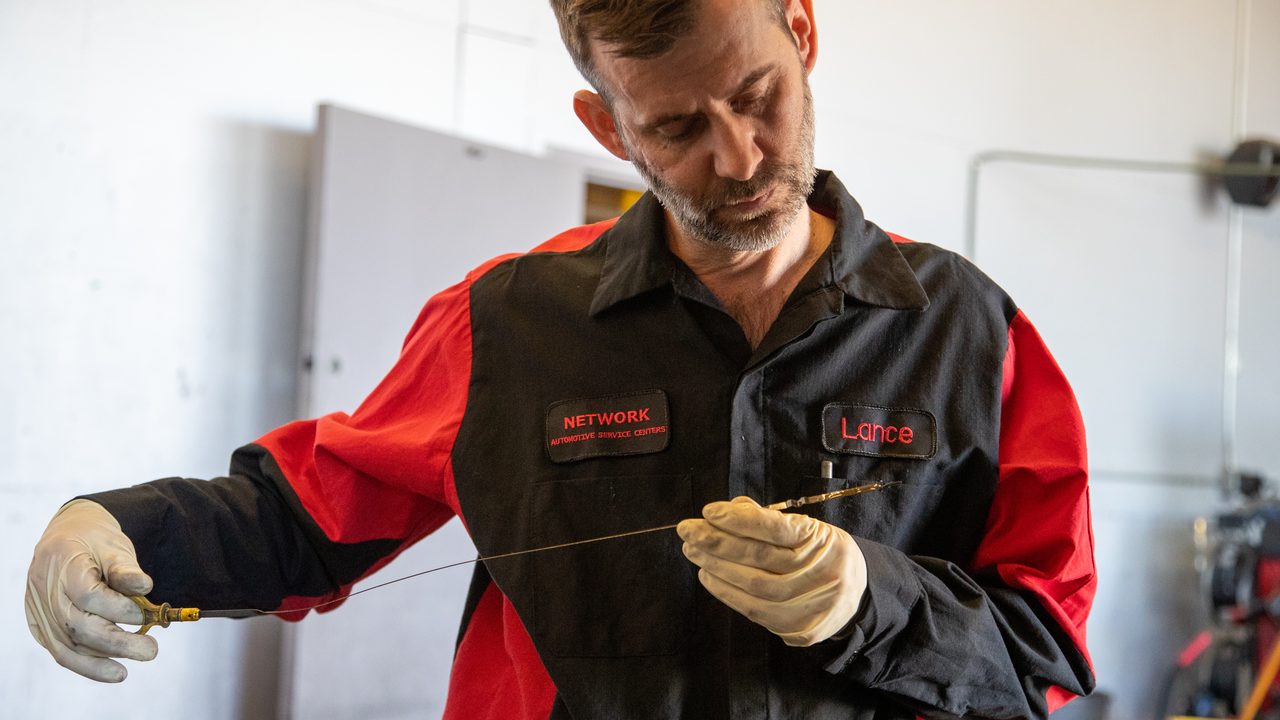 A technician checks the oil level and condition on an engine dipstick in a service bay