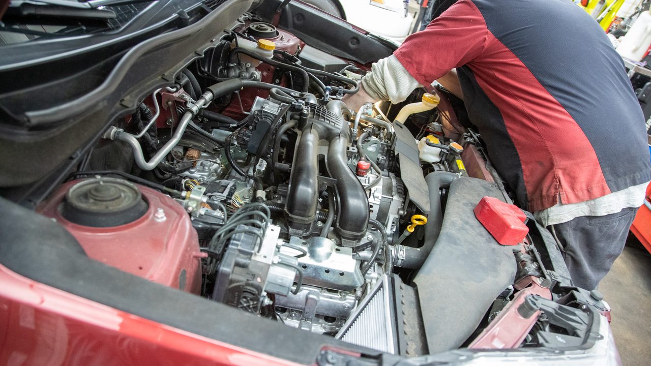 A technician leans into an open engine bay to perform maintenance on a vehicle