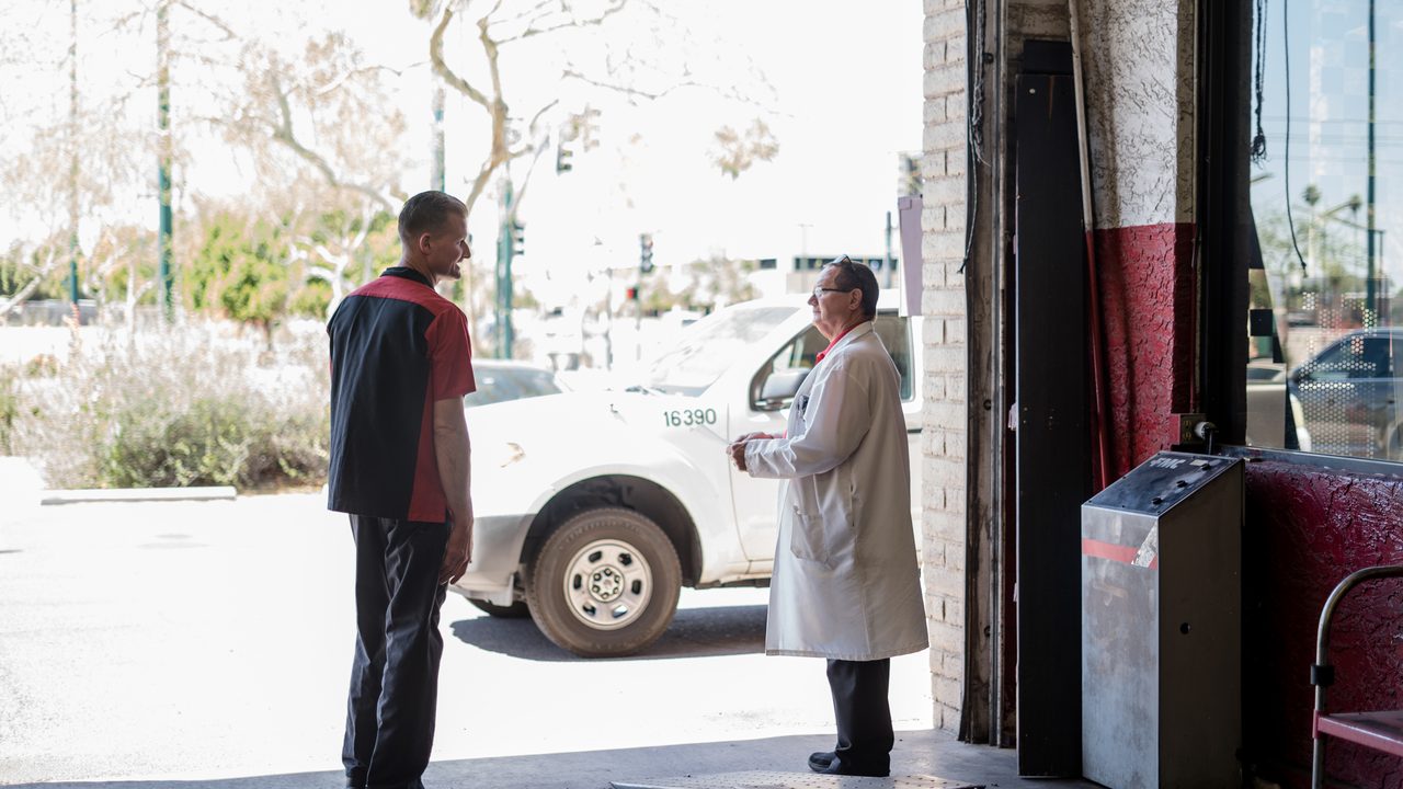 A technician speaks with a shop manager at the entrance of an auto service bay