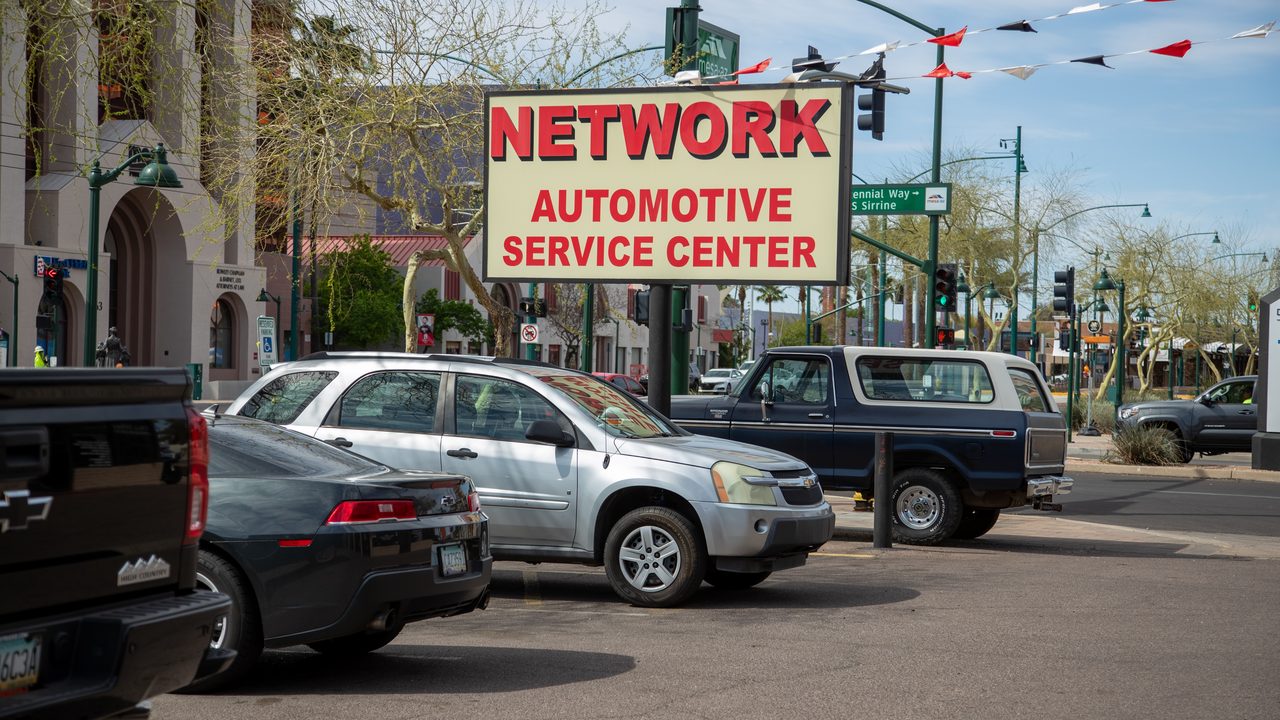 Vehicles parked in an outdoor lot beneath an automotive service center's prominent roadside sign