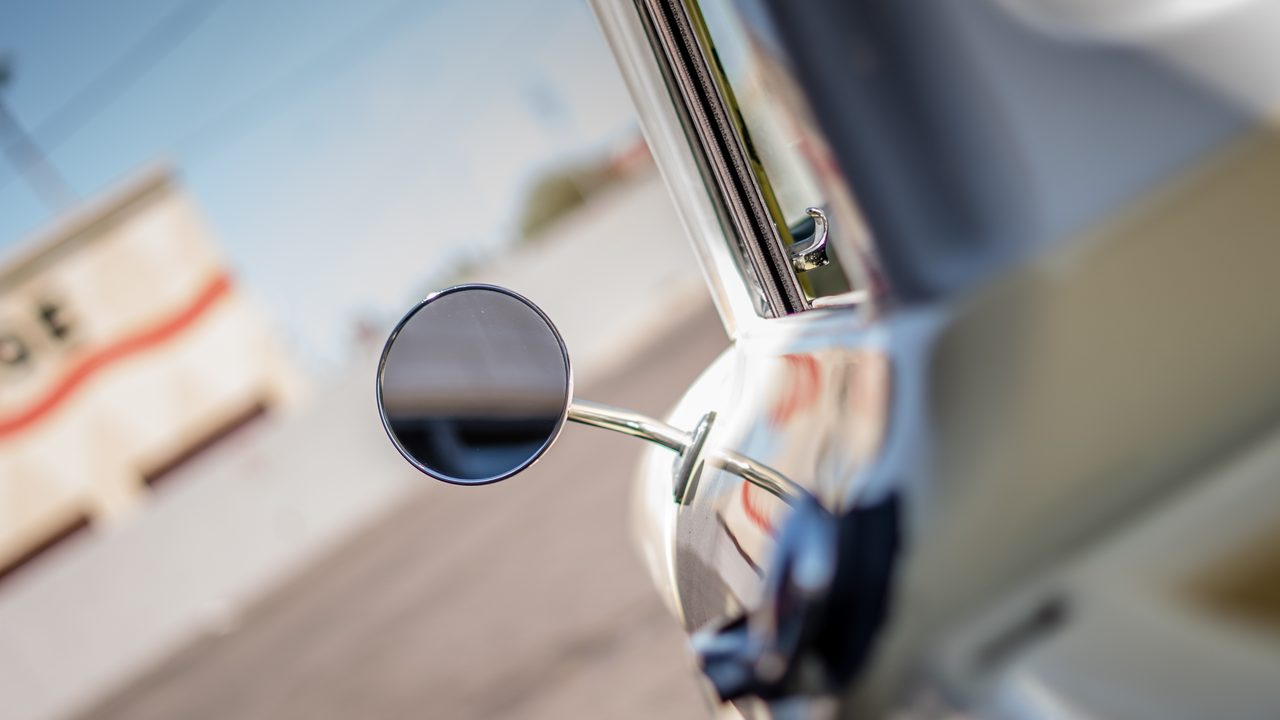 A close-up view along the exterior of a classic car, focusing on its round chrome side mirror