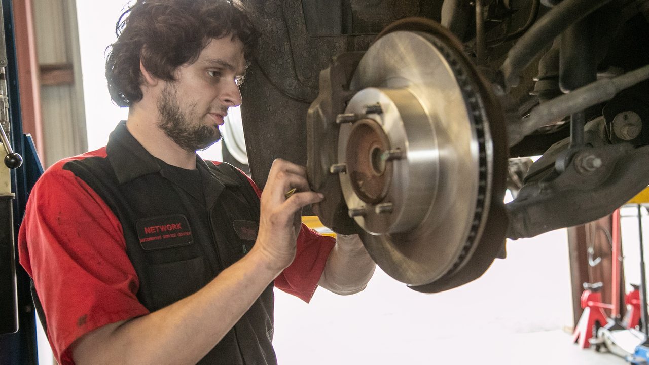 A technician inspects a brake caliper and new brake rotor on a vehicle in a service bay