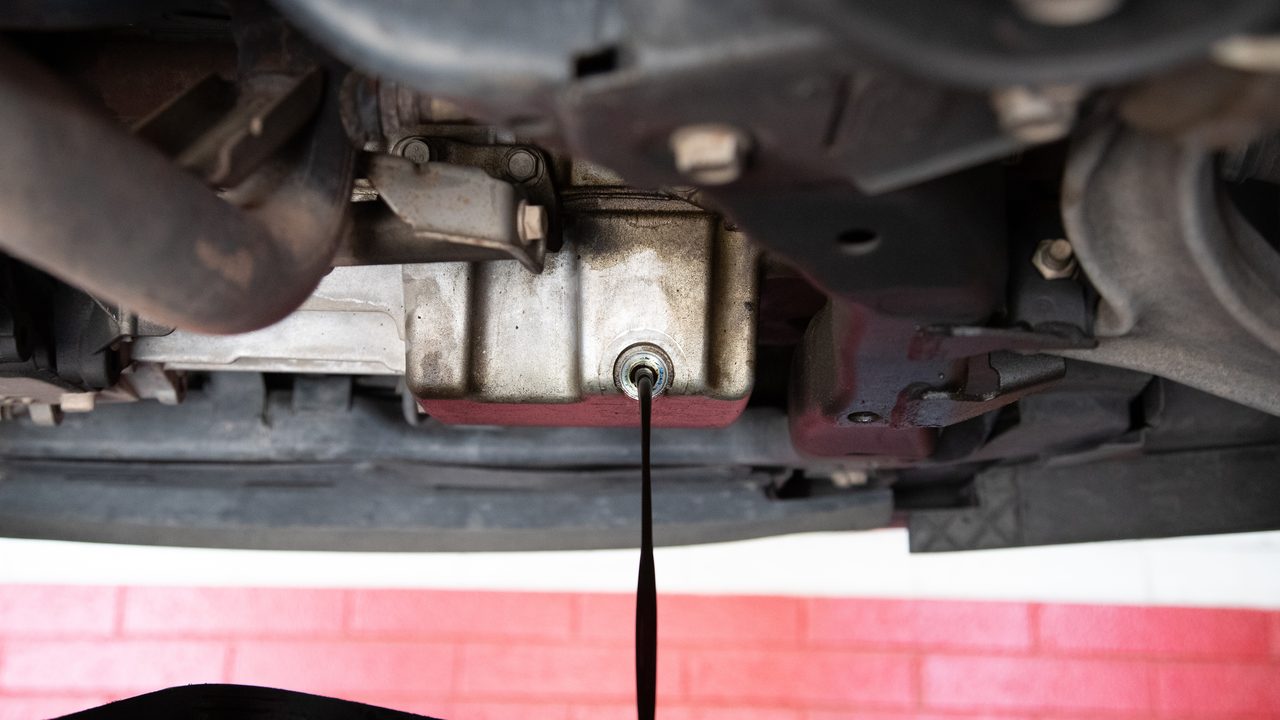 Old engine oil drains from an undercarriage oil pan into a collection container during routine service