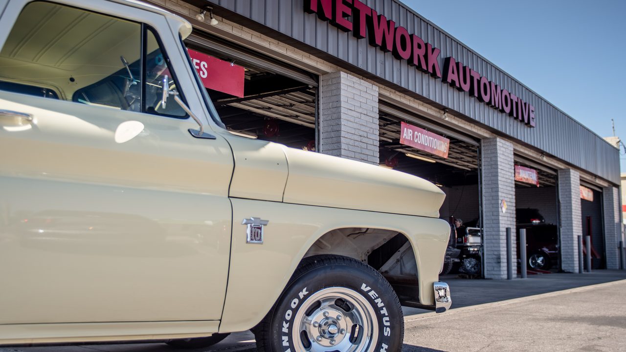 A classic pickup truck is parked outside the service bays of an automotive repair shop