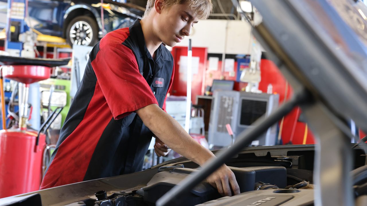A young automotive technician inspects components inside a vehicle's engine bay in an auto repair shop
