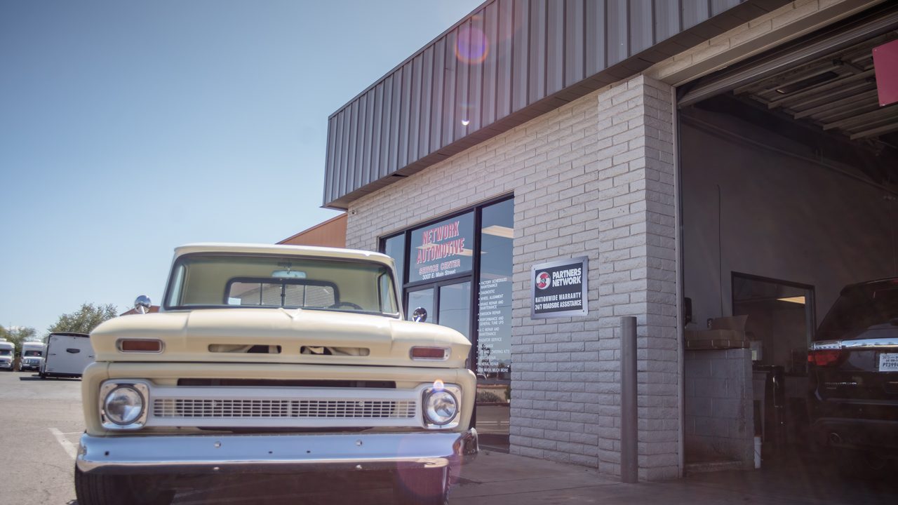 A classic pickup truck is parked outside the storefront and service bay of an auto repair shop