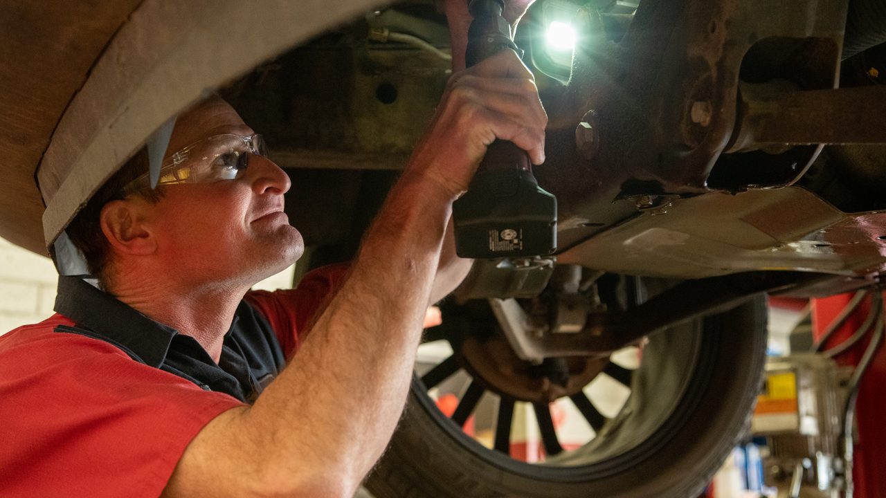 A technician uses a power ratchet with a work light to service a vehicle's undercarriage