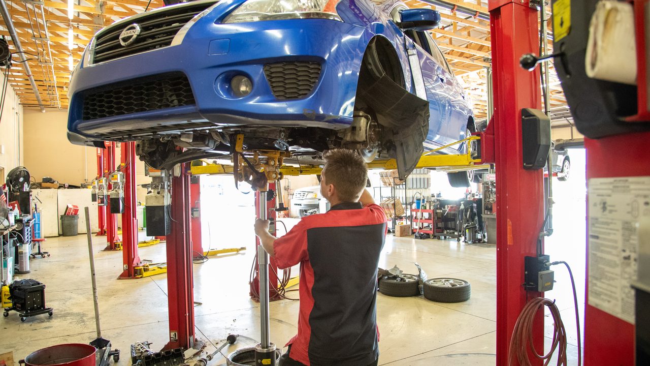 A technician works on the undercarriage of a blue car elevated on a hydraulic lift