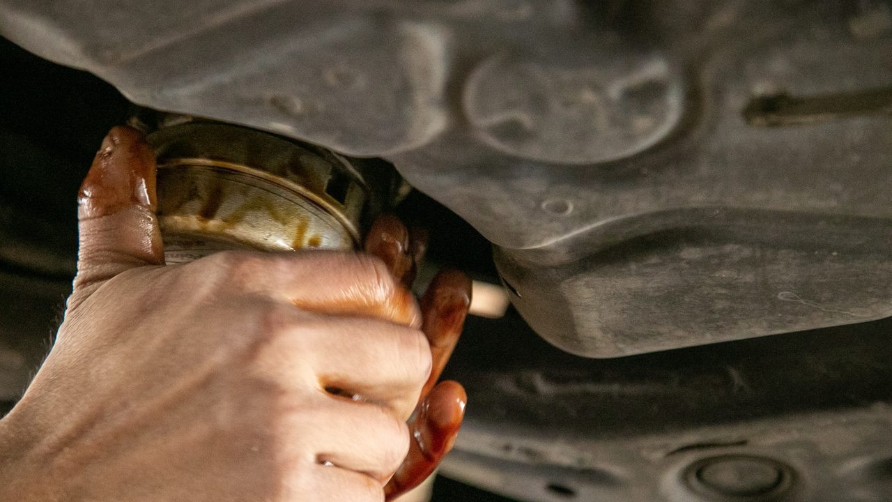 A technician removes an oil filter from the undercarriage of a vehicle during an oil change service