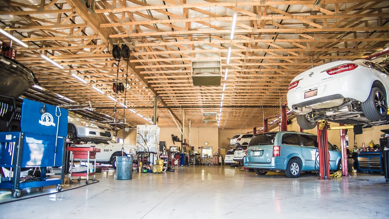 Multiple vehicles are raised on hydraulic lifts inside a spacious auto repair shop service bay