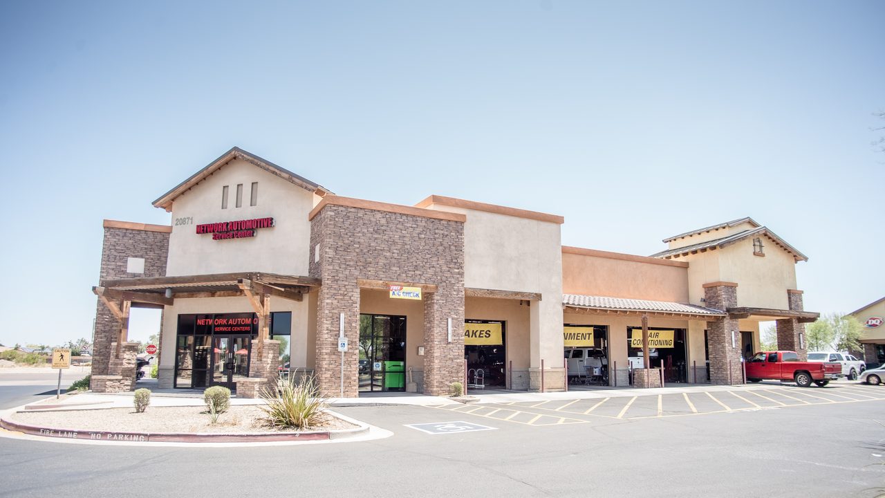The exterior of an automotive repair shop featuring open service bays, signage, and parked vehicles