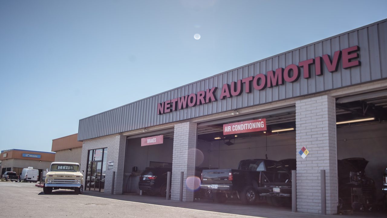 Vehicles sit inside open service bays and parked outside an auto repair shop on a clear sunny day