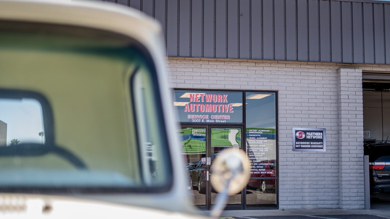 The exterior storefront and service bays of an auto repair shop framed behind a vintage vehicle