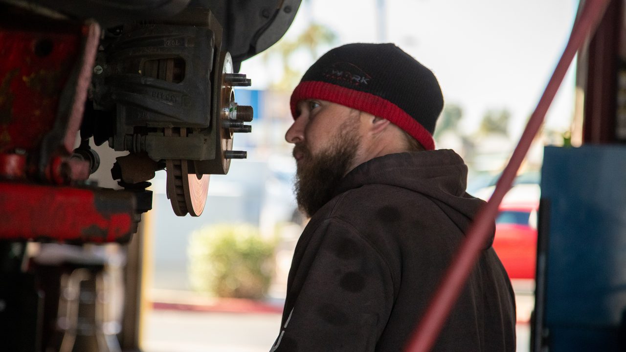 A technician inspects the brake caliper and rotor assembly on a vehicle raised on a lift